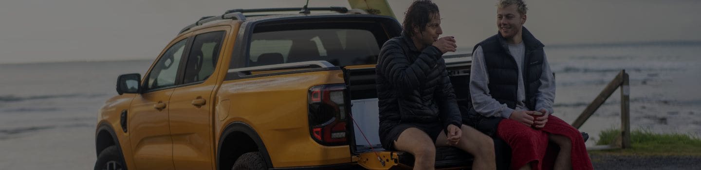 Two men sitting in the back of a Ford Ranger drinking coffee